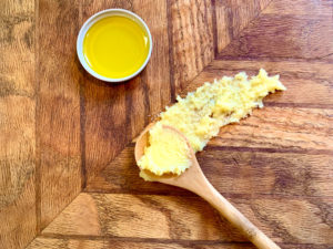 olive oil in a jar cap and ghee in a spoon on a wooden cutting board